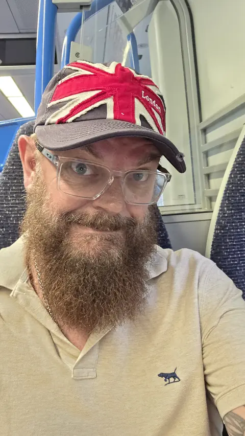 A close portrait of Paul Willard wearing a London cap